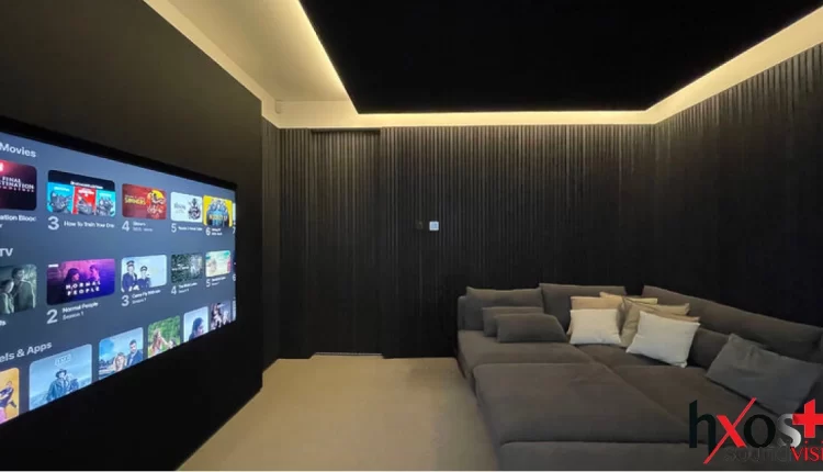 "Μοντέρνος οικιακός κινηματογράφος με μεγάλη τηλεόραση 4K ενσωματωμένη σε minimal design, αόρατα in-wall ηχεία και αιωρούμενη οροφή με ηχεία surround.